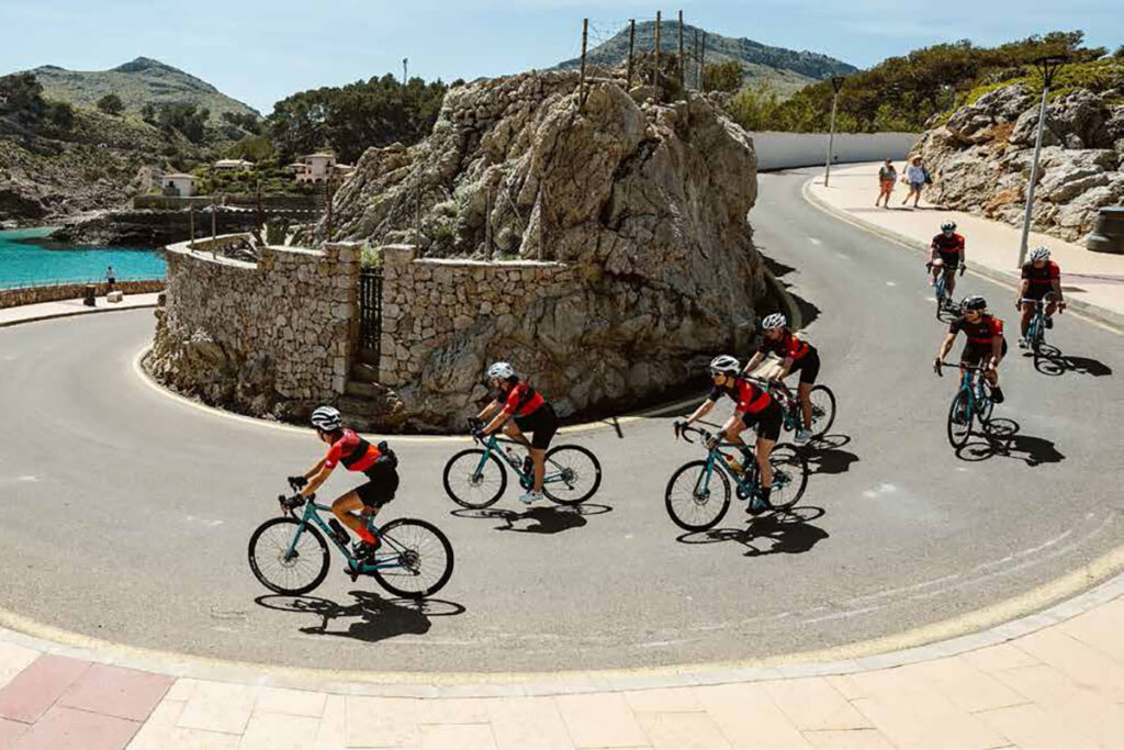 Eine Gruppe von Radfahrern in roten Trikots fährt eine kurvenreiche Straße entlang.
